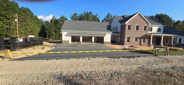 High-quality freshly poured concrete driveway in front of a two-story brick and siding home under construction.